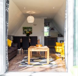 A living room with a wooden coffee table and yellow armchairs near a dining table and kitchen at Valley Lodge 40 in St Ann's Chapel Cornwall