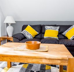 A living room with a wooden coffee table and black sofa with yellow and striped cushions at Valley Lodge 40 in St Ann's Chapel Cornwall