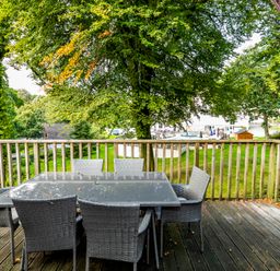 An outdoor wooden deck with a glass-topped table and six wicker chairs surrounded by trees at Valley Lodge 3 St Ann's Chapel Cornwall