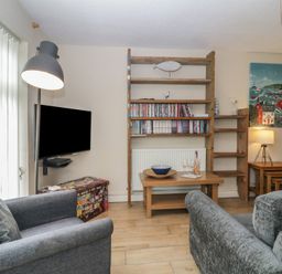 A living room with gray sofas a television mounted on the wall wooden shelves with books and decorations a wooden coffee table and a side table with a lamp at 26 Manorcombe St Ann's Chapel Cornwall