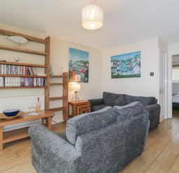 A living room with gray sofas wooden shelves and a wooden table at 26 Manorcombe in St Ann's Chapel Cornwall