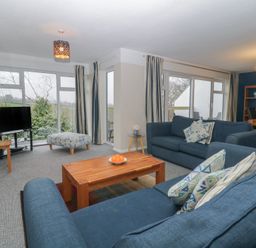 A living room with blue sofas a wooden coffee table and a TV next to large windows at Tamar Cottages 34 St Ann's Chapel Cornwall