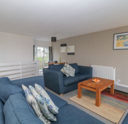 A living room with two blue sofas a wooden coffee table with oranges and framed pictures on the wall at Tamar Cottages 34 in St Ann's Chapel Cornwall