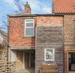 Exterior of a brick and wood house with windows a wooden bench and a gate at Seafield Coach House in Alnmouth