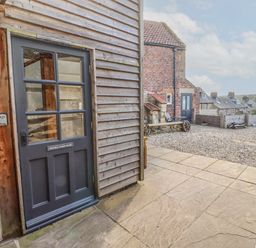 An exterior view of a building with a dark grey door labeled Seafield Coach House on a stone and wood facade at Seafield Coach House in Alnmouth