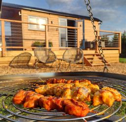 A grill with skewers in front of a cabin with a deck at Fir Tree Shepherd's Hut in Llanon