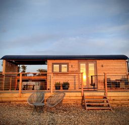 A wooden cabin with a deck and chairs at Fir Tree Shepherd's Hut Llanon