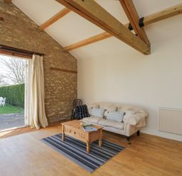 A living room with a sofa a wooden coffee table and open doors leading to a garden at South Barn Cottage in Hatford near Stanford In The Vale