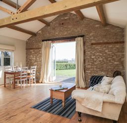A living room with a dining table and chairs wooden beams and an open door to a garden at South Barn Cottage in Hatford near Stanford In The Vale