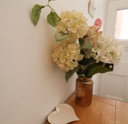 A vase with flowers and a heart shaped dish on a wooden table next to a white door at The Bungalow in Whitby