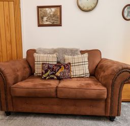 A brown sofa with three cushions in a living room with a wooden door and wall decorations at The Bungalow in Whitby