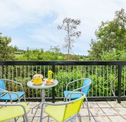 An outdoor balcony with a small round table and four chairs overlooking green trees at Tamar Cottages 35 in St Ann's Chapel Cornwall