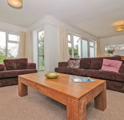 A living room with brown sofas and a wooden coffee table by large windows at Tamar Cottages 35 St Ann's Chapel Cornwall