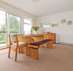 A dining room with a wooden table, chairs, bench, and sliding glass doors opening to a balcony at Tamar Cottages 35 in St Ann's Chapel Cornwall
