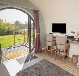 A room with an arched glass door leading outside two chairs at a counter with a mounted television and coffee mugs at The Rowan Pod in Cowbridge