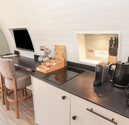 A kitchen counter with a kettle coffee machine knife block and stools next to a wall mounted TV at The Rowan Pod in Cowbridge