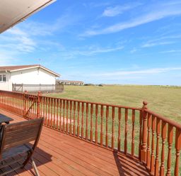 A deck with a table and chairs overlooking a grassy area at Boa Vista in Bacton