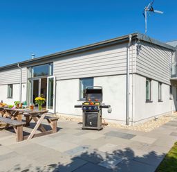 An outdoor patio with picnic tables, food, drinks, and a barbecue grill beside a modern house at Moult Hill Barn in Salcombe
