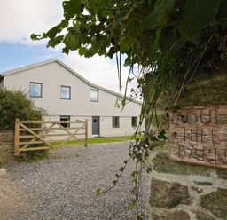 A modern barn-style building with gravel driveway and wooden gate at Moult Hill Barn in Salcombe