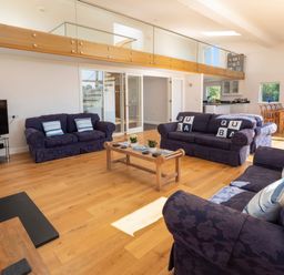 A living room with blue sofas a wooden coffee table and a dining area at Moult Hill Barn in Salcombe
