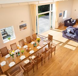 A dining area with a long wooden table set for a meal and a living area with two blue sofas at Moult Hill Barn in Salcombe