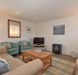 A living room with sofas armchairs a wooden coffee table a television and a small stove at Croft Cottage in Alnwick