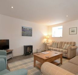 A living room with a striped sofa, two armchairs, a wooden coffee table, a small electric stove, and a television at Croft Cottage in Alnwick