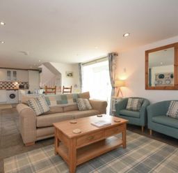 An open plan living room and kitchen with sofas, armchairs, coffee table, dining table, and kitchen appliances at Croft Cottage in Alnwick