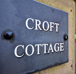 A close up of a black metal plaque with Croft Cottage written on it attached to a stone wall near a green window at Croft Cottage in Alnwick