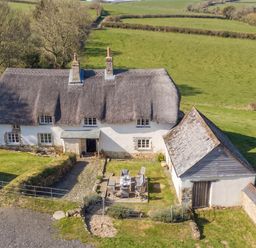 A house with a thatched roof and outdoor seating at Westacombe Farmhouse in Dunsford