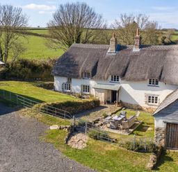 An outdoor area with a thatched roof house and patio furniture at Westacombe Farmhouse in Dunsford