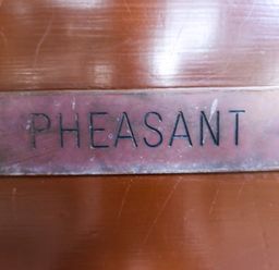 A close up of a metal nameplate with the word PHEASANT on a wooden surface at Pheasant Withern near Alford