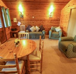 A wooden dining table with chairs and green cushioned armchairs in a wood-paneled room at Pheasant Withern near Alford