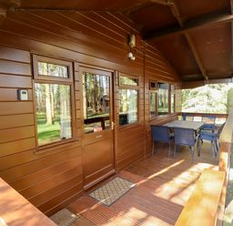 A wooden porch with a table and six chairs outside a cabin in a wooded area at Kestrel Withern near Alford