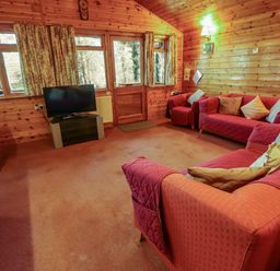 A living room with red sofas a television wooden walls and windows at Kestrel in Withern near Alford