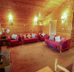 A living room with wooden walls and ceiling with red sofas and armchairs with cushions at Kestrel in Withern near Alford