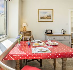 A dining area with a red polka dot tablecloth on a table set with plates cheese and crackers a lamp on a wooden cabinet a bookshelf and a kettle on a counter at Pant Y Cwtsh in Kidwelly