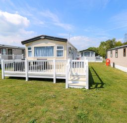 A mobile home with a white railing deck and chairs on grass at Oakley Retreat in Fritton near Belton