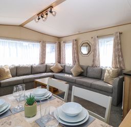 A living room with a long gray sofa and a dining table set with dishes glasses and a small plant at Oakley Retreat in Fritton near Belton