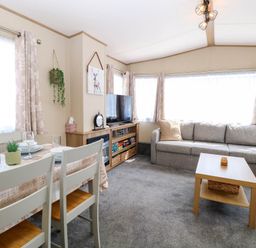 A living room with a gray sofa a wooden coffee table a dining table with chairs and a television on a cabinet at Oakley Retreat in Fritton near Belton
