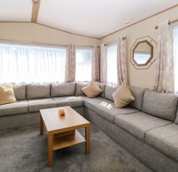 A living room with a gray corner sofa beige cushions a wooden coffee table and windows with curtains at Oakley Retreat in Fritton near Belton