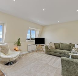 A living room with green sofas a white chair and windows showing sea views at No 10 Croft House in Tenby