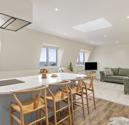 A living area with a kitchen island and wooden stools and green sofas with a TV and windows overlooking the sea at No 10 Croft House in Tenby