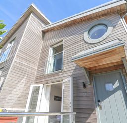 Exterior of a modern wooden house with a blue door and balcony at Azure Retreat at Una in Carbis Bay near St Ives