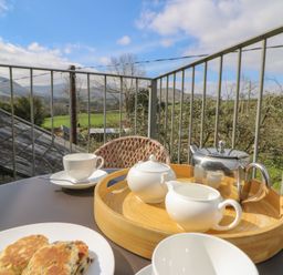 A balcony with a table set for tea including a teapot, cup, and plate of scones with countryside views at Cantref House Top Floor in Brecon
