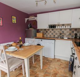 A kitchen with wooden table and chairs set for two with appliances and cabinets against purple walls at Cantref House Top Floor in Brecon