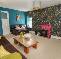 A living room with a brown sofa and a leather loveseat a wooden coffee table a floral wallpapered wall with a pink fireplace at Cantref House Top Floor in Brecon