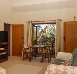 A sitting room with a small wooden table and chairs a TV and sofa open doors showing a horse outside at The Dairy at Wyke Farm  Wyke near Lyme Regis