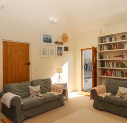 A living room with two sofas a lamp a bookshelf and an open door at The Dairy at Wyke Farm Wyke near Lyme Regis
