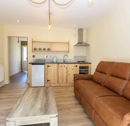 A living room with a sofa, table and kitchen area at Barn Owl Lodge
